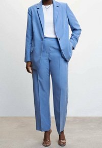 Costume bleu clair sur mesure comprenant un blazer à un bouton et un pantalon à jambes larges, réalisé dans un tissu lisse au design minimaliste.