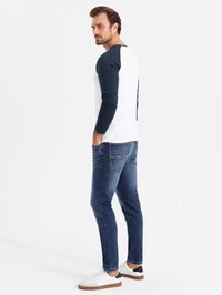 Hvid skjorte med lange ærmer og marineblå raglanærmer, parret med mørk denim jeans og hvide sneakers med brune såler. Glat tekstur, afslappet pasform.