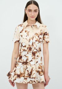 Kortärmad, beige klänning med blommiga bruna mönster, krage, knapp-up front och utsvängd kjol. Har framfickor och ett bälte.