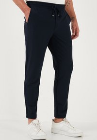 Marine joggingsbroeken met een trekkoord in de taille, zijzakken, taps toelopende pijpen en gladde stof. Gemaakt met witte sneakers.