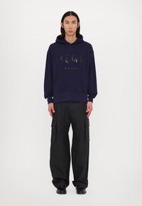 Felpa navy con logo nero "MSGM MILANO" sulla parte frontale; abbinata a pantaloni cargo neri. Tessuto liscio, cordoncino regolabile sul cappuccio.