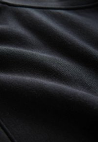 Zwarte stof met een gladde textuur, die zachte plooien en een lichte glans laat zien. Het materiaal lijkt lichtgewicht, geschikt voor kleding.