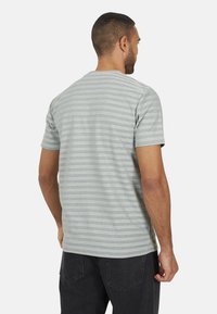 T-shirt gris à rayures, manches courtes, en tissu léger. Présente des rayures horizontales claires et foncées, un col rond et une coupe décontractée.