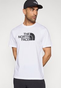 Λευκό βαμβακερό T-shirt με κοντά μανίκια, με μεγάλο μαύρο λογότυπο «THE NORTH FACE» στο μπροστινό μέρος. Απλό και κλασικό κόψιμο.