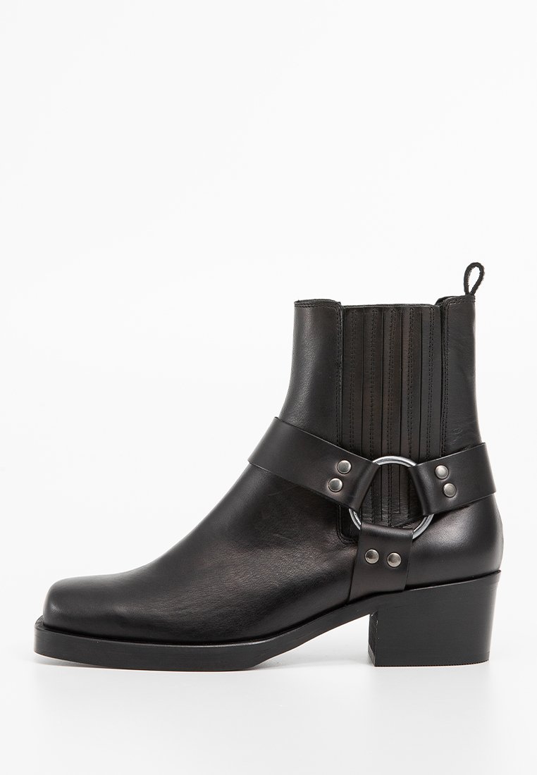 Stivale alla caviglia in pelle nera con punta arrotondata, inserti elasticizzati a coste e una fibbia decorativa in metallo. Design con tacco a blocco per una maggiore stabilità.
