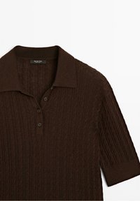 Polo en maille marron à manches courtes avec motif torsadé, trois boutons et col, posé à plat sur fond blanc.
