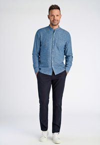 Camicia in chambray blu con colletto alla coreana, taschino sul petto e chiusura con bottoni. Abbinata a pantaloni blu navy e sneakers bianche.