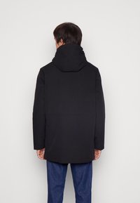 Abrigo negro con capucha de corte recto, con una textura suave y sin patrones visibles, llevado sobre pantalones de mezclilla azul.