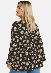 Blusa nera floreale con rose rosa, maniche a campana e orlo peplum. Tessuto morbido con una vestibilità comoda e dettaglio arricciato sul retro.
