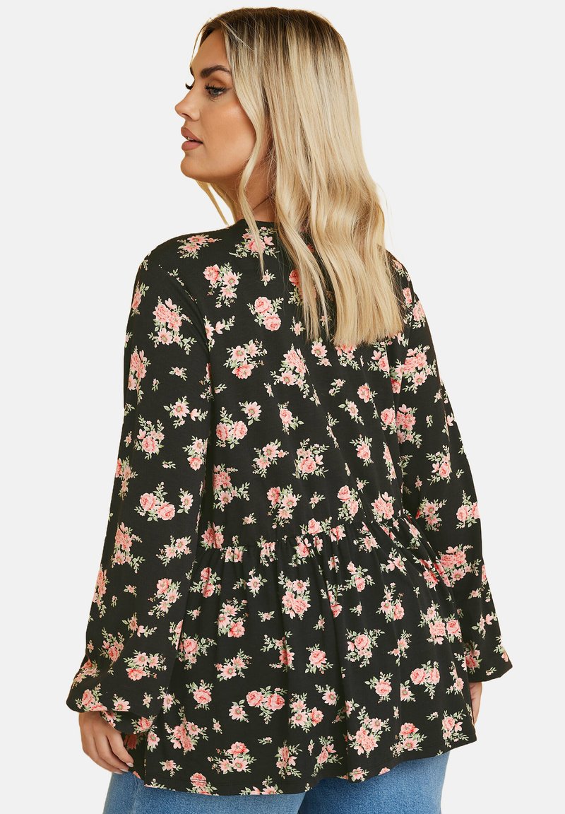 Blusa nera floreale con rose rosa, maniche a campana e orlo peplum. Tessuto morbido con una vestibilità comoda e dettaglio arricciato sul retro.