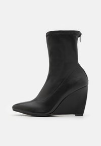 Botte de cheville noire à talon en forme de coin avec un bout pointu, en cuir lisse, fermeture à glissière, et une silhouette élégante, avec des accents cousus.