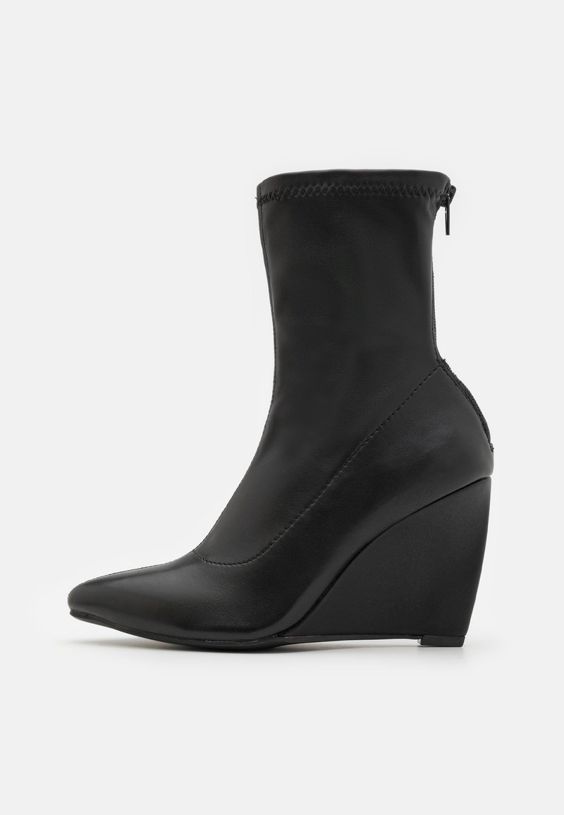 Botte de cheville noire à talon en forme de coin avec un bout pointu, en cuir lisse, fermeture à glissière, et une silhouette élégante, avec des accents cousus.
