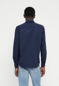 Tumesinine pikkade varrukatega särk valgete geomeetriliste mustritega, klassikalise krae, nööbitavate mansettide ja sirge alläärega.