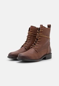 Bottes en cuir marron avec un bout rond, un design à lacets et un talon bas empilé. Présentent une texture lisse et des détails de couture minimaux.