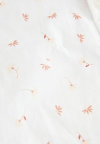 Tissu léger avec un fond blanc orné de motifs floraux éparpillés dans des teintes douces de rose et de rouge. Texture lisse, design délicat.