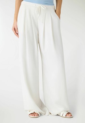 Pantaloni bianchi a gamba larga e vita alta con coulisse in vita e tasche laterali, indossati con sandali bianchi open-toe e top azzurro chiaro.