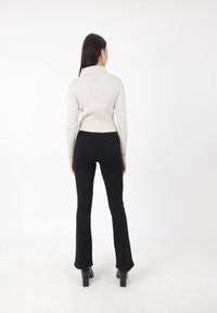 Witte geribde coltrui in combinatie met zwarte flare jeans en zwarte plateau laarzen, gezien van achteren tegen een witte achtergrond.