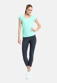 Top corto verde menta abbinato a leggings capri neri e scarpe da ginnastica bianche. Design liscio e aderente, adatto per l'abbigliamento sportivo.