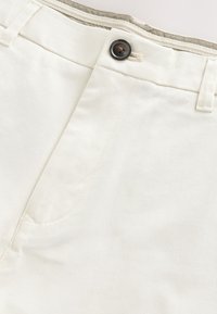 Pantaloni bianchi di cotone con chiusura a bottone in vita, texture liscia e dettaglio di cucitura sottile lungo la tasca anteriore.