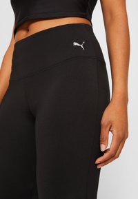 Černé sportovní legíny s vysokým pasem, s malým stříbrným logem Puma a prošitím podél švů. Hladká textura.