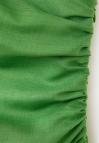Gros plan d'un tissu vert avec une texture de tissage visible et des plis rassemblés le long d'un bord.