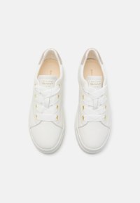 Weiße Ledersneaker mit flachen weißen Schnürsenkeln und goldenen Hardware-Akzenten. Runde Zehenform, gepolsterter Innenraum und ein samtiger Fersenbereich.