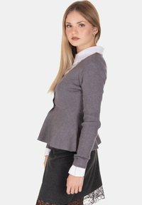 Top peplum grigio a coste con colletto bianco, abbinato a una gonna a tubino scura con orlo in pizzo. Il design è sagomato e strutturato.