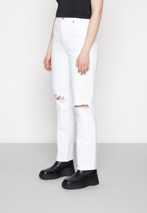 Jeans de ganga branca com rasgos desgastados nos joelhos, design de cintura alta, corte reto e detalhes de costura mínimos, usados com sapatos pretos robustos.