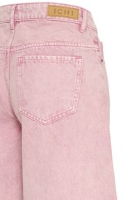 Bagside af lyserøde denimjeans med en enkelt baglomme og en tan-farvet læderlap mærket "ICHI" på linningen.