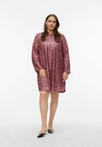 Lyserød pailletkjole med lange ærmer, løs pasform og rund halsudskæring. Kombineret med mørkfarvede spidse flade sko og minimal smykning.