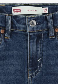 Levi's 511 Slim jeans in dark denim. Features a silver button, copper rivets, and contrasting yellow stitching. Size 12 tag visible.