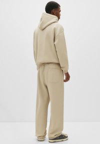 Beige hoodie en bijpassende joggingbroek van zachte stof. Hoodie ontwerp met een buidelzak, losse pasvorm en zichtbare stikdetails.