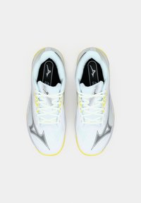 White athletic shoes with yellow accents, textured upper, black logo, and lace-up design. Features a sleek, modern silhouette.