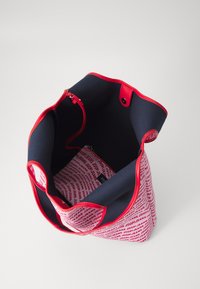 Platnena torba z rdečimi detajli, z mornarsko modrim notranjim delom. Notranjost ima žep z zadrgo z večkratno blagovno znamko rdeče na belem.