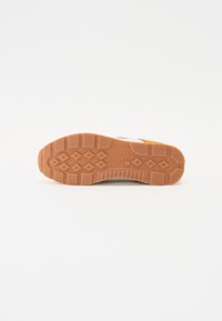 Hnědá gumová podrážka s texturovanými drážkami a diamantovými vzory; obsahuje bílou svrškovou část s minimalistickým detailem a zaoblenou špičkou.