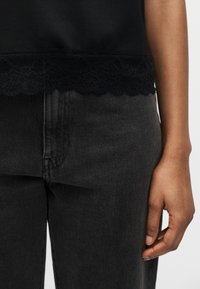 Το δεξί χέρι ξεκουράζεται δίπλα σε μαύρο τζιν και μαύρο τοπ με δαντέλα στο τελείωμα.