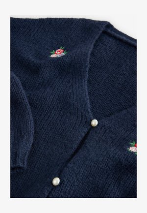 Navy zilā adīta kardigāna jaciņa ar V-veida kaklu, pērļu pogām un ziedu izšuvumiem ar rozā un zaļām akcentiem. Mīksta tekstūra un vidēja biezuma.