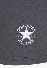 Szara tkanina z teksturowanym wzorem, z białym haftowanym logo „Converse All Star” i wzorem gwiazdy blisko dołu.