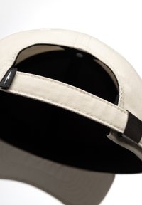 Beige katoenen pet met een verstelbare donkere band, zwarte binnenvoering en een gestructureerde kroon. Voorzien van stiksels en een klein logolabel.