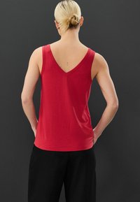 Top senza maniche rosso in tessuto morbido con scollatura a V nella parte posteriore e vestibilità comoda, abbinato a pantaloni neri larghi.