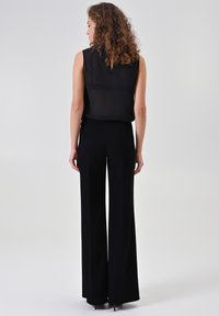 Zwart doorschijnend mouwloos topje gecombineerd met zwarte textuur-broek met wijde pijpen. De broek heeft een subtiel visgraatpatroon en een hoge taille.