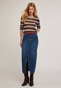 Suéter de punto con rayas horizontales en beige y azul marino, combinado con una falda larga de mezclilla azul con una abertura frontal y un cinturón rojo. Botas de serpiente marrón.