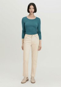 Türkises Langarmshirt, cremefarbene gerade Hosen und beige Slipper. Glattes Material und schlichtes Design, keine sichtbaren Muster oder Akzente.
