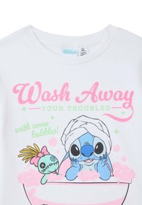 T-shirt bianco in cotone con una caricatura in vasca, accompagnata da un testo rosa che recita "Lavare via i problemi" e bolle intorno.