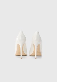Λευκά γυναικεία παπούτσια με ψηλό τακούνι και λεία, γυαλιστερή επιφάνεια, μυτερή μύτη και λεπτά τακούνια. Στο εσωτερικό διαθέτουν λεπτομέρειες με το λογότυπο της μάρκας.
