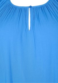 Blå blus med lös passform och rynkad textur. Har en rund halsringning och en bakre stängning med en knapp.