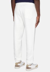 White sweatpants with an elastic waistband, featuring a single rear pocket. The fabric appears soft, paired with white and beige sneakers.