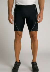 Shorts de cyclisme noirs avec insert rembourré, dotés d'un design ajusté et de coutures latérales grises. Portés avec des chaussures de cyclisme noires.