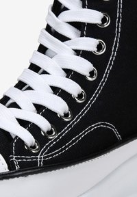 Sneaker alta nera in canvas con occhielli e lacci bianchi. Presenta cuciture bianche e una suola in gomma, evidenziando un design classico.