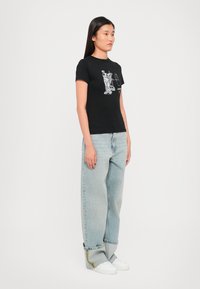 Svart bomull T-skjorte med hvite grafiske trykk. Kombinert med løse lyseblå jeans og hvite joggesko. Enkel, uformell design.